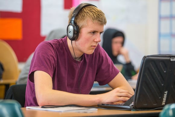 A person wearing headphones works on a laptop in a classroom. NZQA link